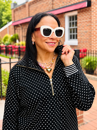 A black long-sleeve top with white polka dots and a gold zipper at the collar