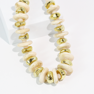 A chunky statement necklace featuring alternating smooth cream-colored disc beads and textured metallic gold disc beads.