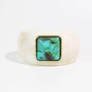 A wide, chunky cuff bracelet made of cream-colored marbled resin, featuring a square bezel-set green and turquoise marbled stone inlay with a gold-tone border.