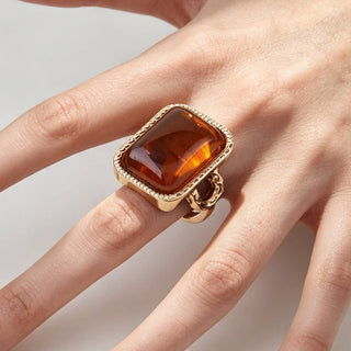 A tortoise marble stone ring with a smooth polished stone encased in twisted textured metal, worn on a finger.