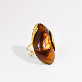 A gold ring featuring a large, organic-shaped amber cabochon with a glossy, warm brown color and natural inclusions.