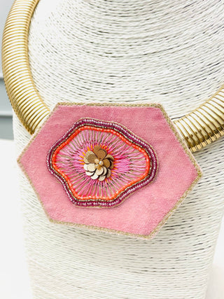 A pink hexagonal fabric pendant with intricate floral embroidery, sequins, and beadwork on a gold choker chain.