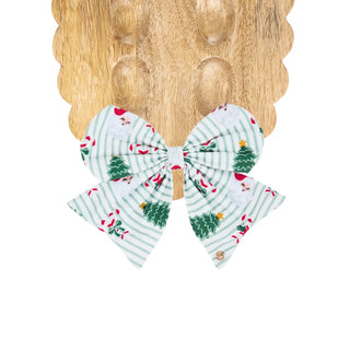 A large magnetic bow with light green vertical stripes and a Christmas print featuring green trees, red hats, and small red accents.