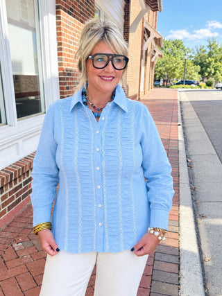  Easel blue blouse with button-down features, a classic collar, ruffled pintuck detailing, delicate lace trim, and an elastic smocked waist at the back