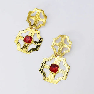 A pair of gold-tone hammered dangle earrings with a central red cushion-cut gemstone.