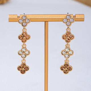 A pair of gold-tone drop earrings. Each earring has a four-petal flower cluster at the top with pale gray stones, followed by three dangling four-petal clusters with alternating gold and clear rhinestones.
