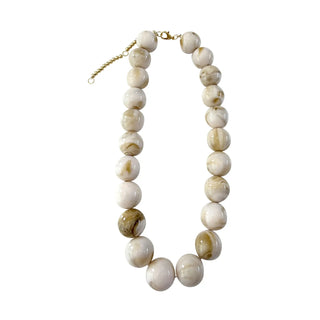 A beaded necklace made of large, round, polished stone beads in cream, beige, and light brown with natural marbling, finished with a gold-tone extender chain and clasp.