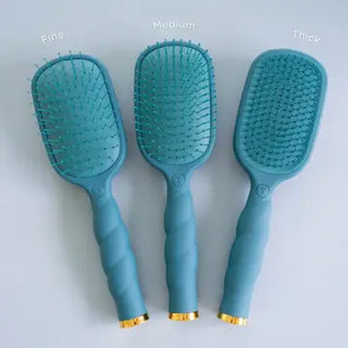 Telelties three detangler Teal With It hairbrushes with twisted handles and gold metal accents at the base.