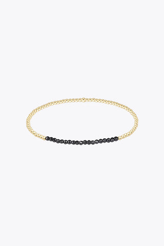 A slim stretch bracelet composed of small 14K gold filled beads with a section of faceted black hematite beads at the front y Enewton.