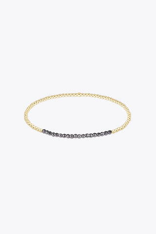 A delicate 2mm stretch beaded bracelet featuring 14K gold filled round beads with a section of smaller dark faceted hematite beads along the bottom arc by Enewton.
