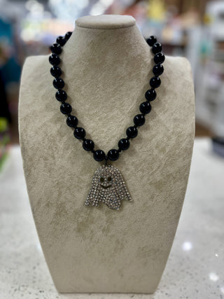 A black beaded necklace with a rhinestone-encrusted ghost pendant, displayed on a textured beige jewelry bust.