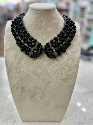 A multi-strand black beaded collar necklace displayed on a textured cream-colored mannequin bust.