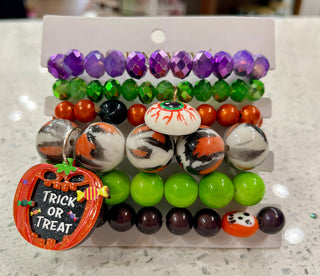 A set of Halloween-themed beaded bracelets. The bracelets feature purple faceted beads, green beads, orange and black beads, marbled orange, black, and white beads, bright green beads, dark purple beads, and a small pumpkin-shaped charm that reads 'TRICK OR TREAT'.