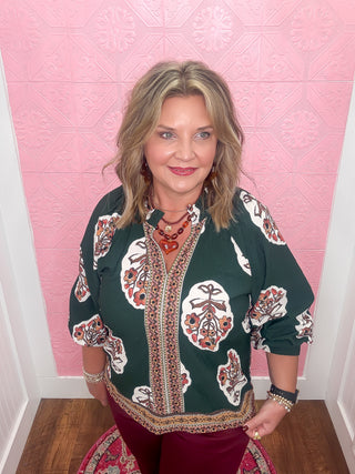 Woman wearing a patterned top against a pink textured wall.
