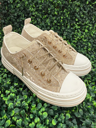 A pair of low-top platform sneakers in a gold glittery fabric with a subtle leopard print pattern, featuring chunky white soles and rhinestone no tie  laces