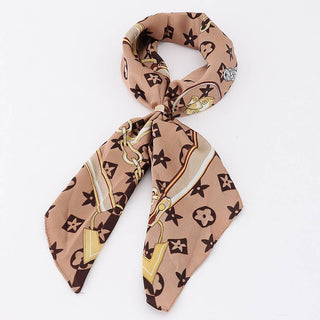 A beige silk scarf with a brown and gold  pattern, tied in a loop with gold ring.