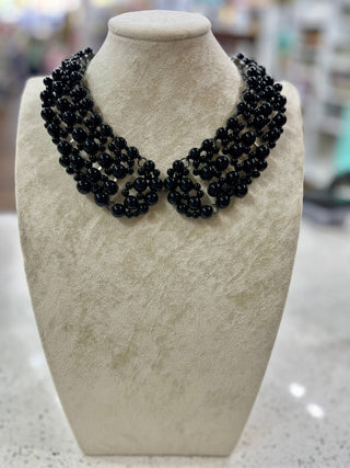 A multi-strand black beaded collar necklace displayed on a textured cream-colored mannequin bust.
