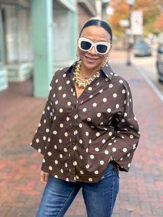 Cocoa Charm Blouse is an oversized polka dot button-down in a warm cocoa palette with wide dolman sleeves finished with buttoned cuffs, a classic pointed collar, and a dramatic high-low hem