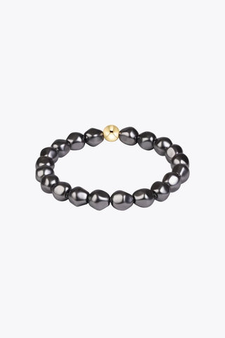 A stretch bracelet composed of dark grey baroque-style beads with a single polished gold-tone round accent bead made by Enewton.