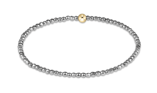A stretch bracelet composed of small faceted silver-tone hematite beads with a single smooth gold-tone accent bead by Enewton.