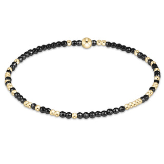 A thin stretch beaded bracelet with small faceted black hematite beads and evenly spaced polished gold-tone round accent beads by Enewton.