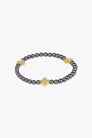 A stretch beaded bracelet featuring small dark grey pearl beads and three evenly spaced 14K gold filled crosses by Enewton.
