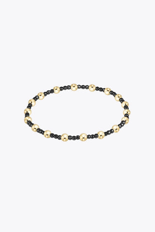 A beaded stretch bracelet featuring small faceted black hematite beads alternating with larger 14K gold filled beads on a stretch cord by Enewton.