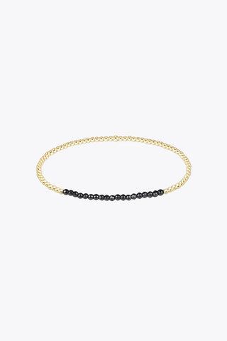 A slim stretch bracelet composed of small 14K gold filled beads with a section of faceted black hematite beads at the front y Enewton.
