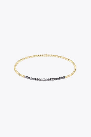 A delicate 2mm stretch beaded bracelet featuring 14K gold filled round beads with a section of smaller dark faceted hematite beads along the bottom arc by Enewton.