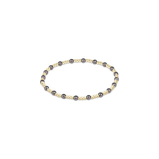 A stretch beaded bracelet featuring small 14K gold-filled beads interspersed with larger dark grey pearl crystal beads by Enewton.