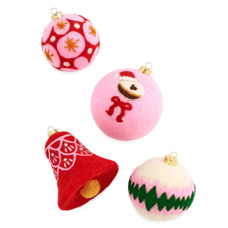 Four felt Christmas ornaments on a white background: a red ornament with white floral patterns and gold star accents, a pink ornament with a small face and red bow, a red bell ornament with white patterns and gold trim, and a cream ornament with green and pink zigzag stripes and a gold cap.
