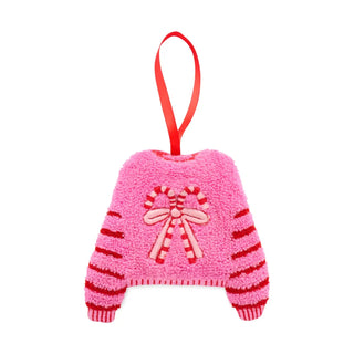 A pink fuzzy Christmas ornament shaped like a sweater, with red and pink striped sleeves, a candy cane motif on the chest, and a red hanging ribbon.