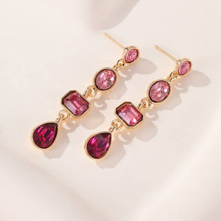 A pair of gold-plated drop earrings featuring pink gemstones in oval, rectangular, and teardrop shapes.