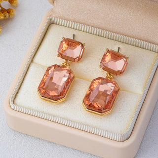 A pair of gold-tone drop earrings with large peach-orange faceted rectangular gemstones.