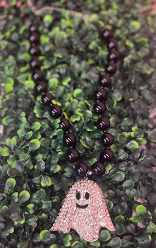A beaded necklace with glossy  black beads and a rhinestone-encrusted ghost pendant, displayed on green foliage.