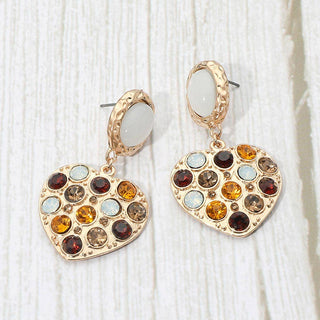 A pair of gold hoop earrings with dangling heart-shaped charms embellished with multiple round gemstones in amber, brown, and autumn colors.