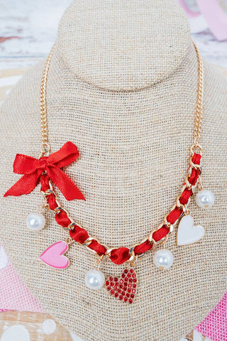 Necklace with red bows, heart shapes, and pearl charms. 
