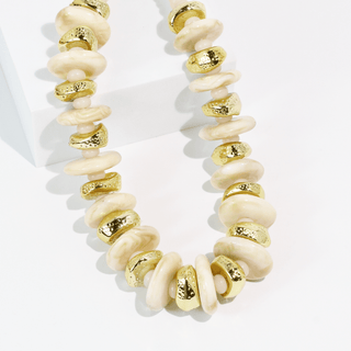 A chunky statement necklace featuring alternating smooth cream-colored disc beads and textured metallic gold disc beads.