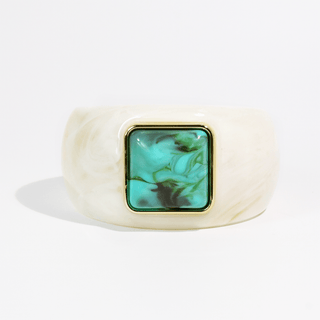 A wide, chunky cuff bracelet made of cream-colored marbled resin, featuring a square bezel-set green and turquoise marbled stone inlay with a gold-tone border.