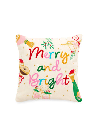 A square decorative throw pillow with a cream background, featuring the words 'Merry and Bright' in multicolored script, surrounded by festive illustrations including mistletoe, bells, ornaments, and a green stocking.