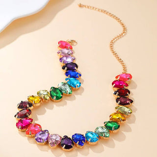 A gold-tone chain necklace featuring a series of colorful, teardrop-shaped rhinestones in pink, purple, blue, green, yellow, and red.
