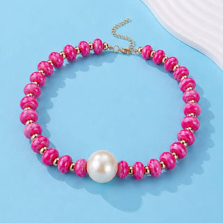 A beaded necklace featuring textured fuchsia colored marbled beads, small gold spacer beads, a large white pearl at the center, and a gold-tone chain clasp.