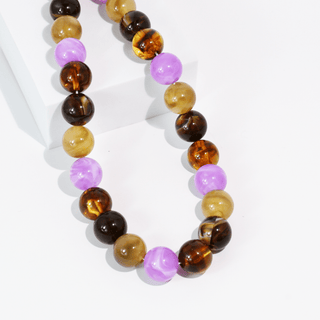 A beaded necklace made of polished round gemstone beads in amber brown, dark brown, light tan, and lavender purple.
