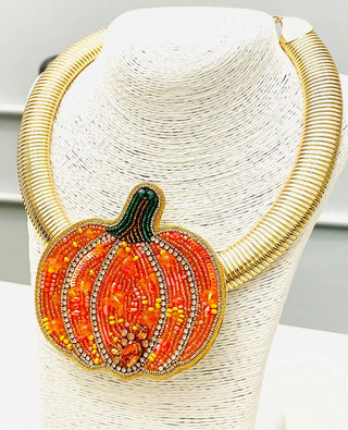 A gold-toned beaded choker necklace with a large pumpkin-shaped pendant.