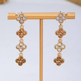 A pair of gold-tone drop earrings. Each earring has a four-petal flower cluster at the top with pale gray stones, followed by three dangling four-petal clusters with alternating gold and clear rhinestones.
