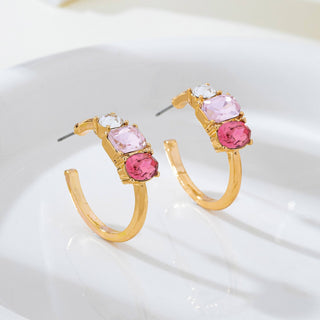 A pair of gold hoop earrings with three stacked gemstones in each earring: a clear round stone, a light pink oval stone, and a larger pink oval stone. 