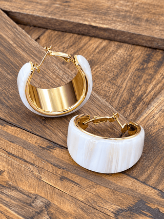 A pair of gold hoop earrings with thick, rounded ivory resin outer shells.