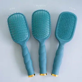 Telelties three detangler Teal With It hairbrushes with twisted handles and gold metal accents at the base.