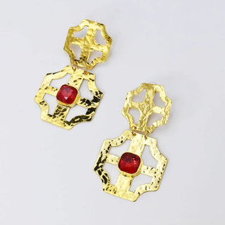 A pair of gold-tone hammered dangle earrings with a central red cushion-cut gemstone.